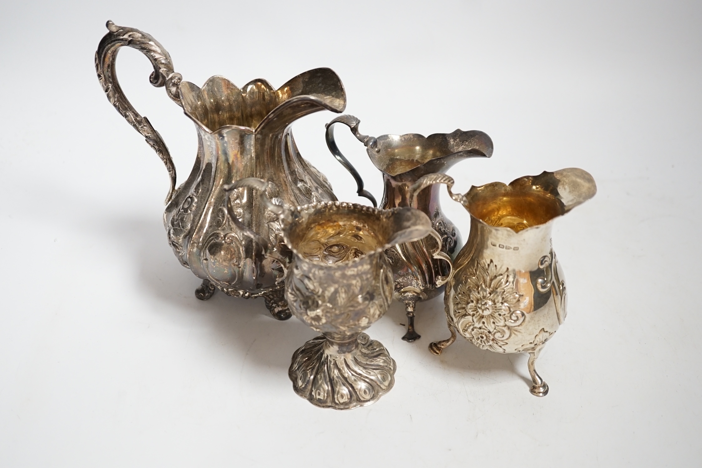 A George III inverts pear shaped cream jug with later embossed decoration, 11.2cm and three later silver cream jugs including two Victorian, 17.4oz.